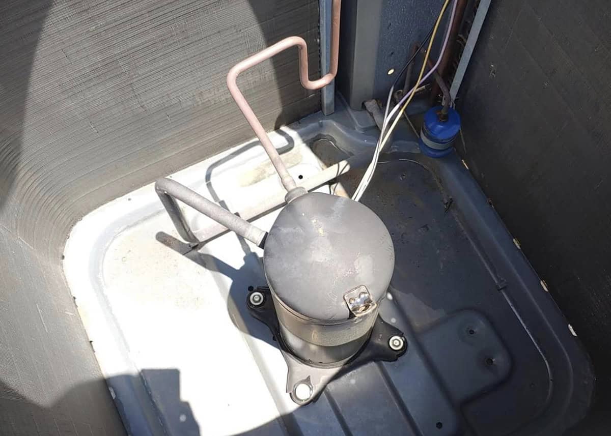 Inside view of an outdoor AC condenser showing the compressor unit during HVAC repair
