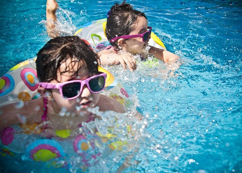 Two children enjoying swimming pool on hot summer day in Terrell Texas with reliable home AC cooling