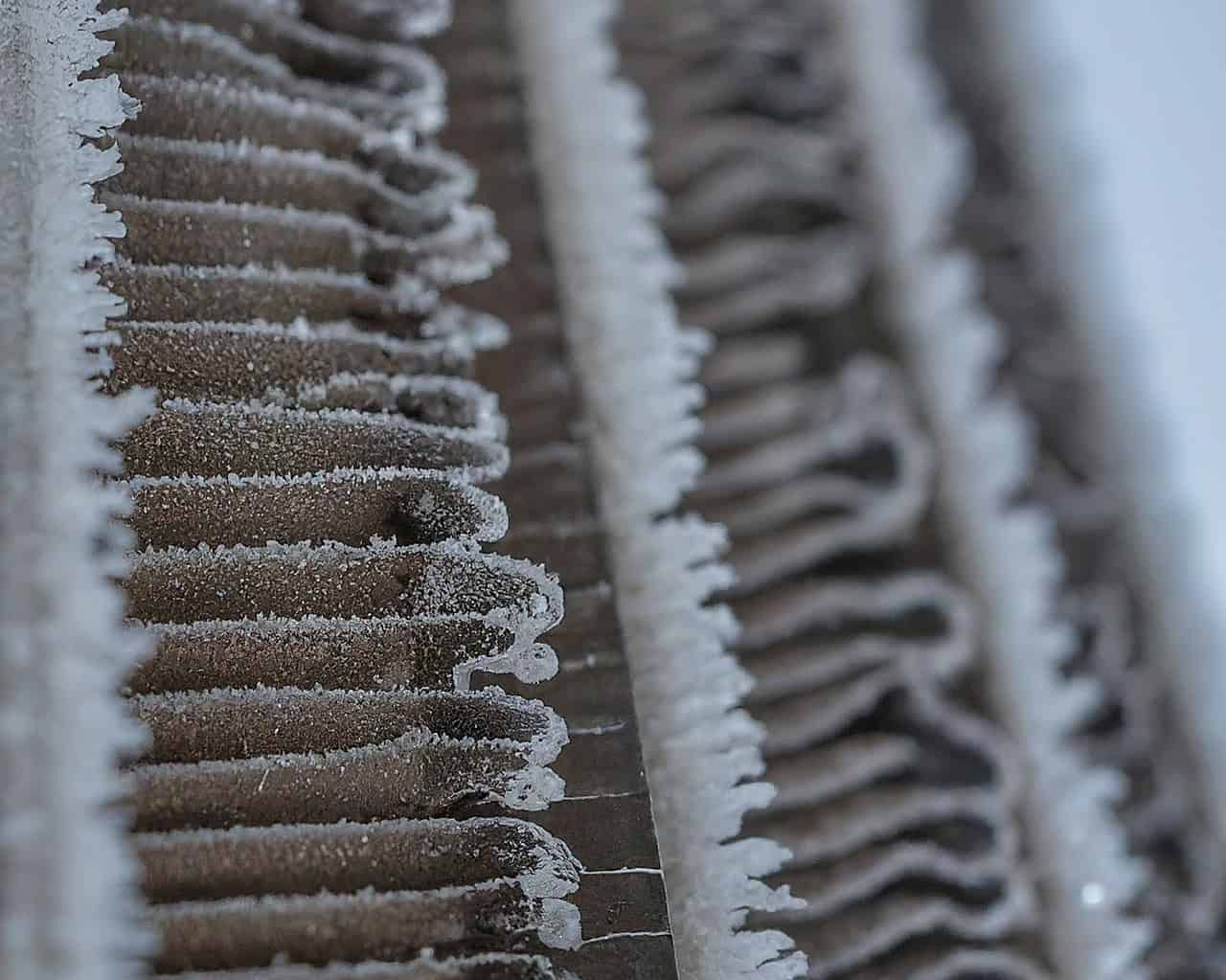 Frozen heat pump evaporator coil covered in frost and ice buildup, restricting airflow and reducing heating efficiency in cold weather.