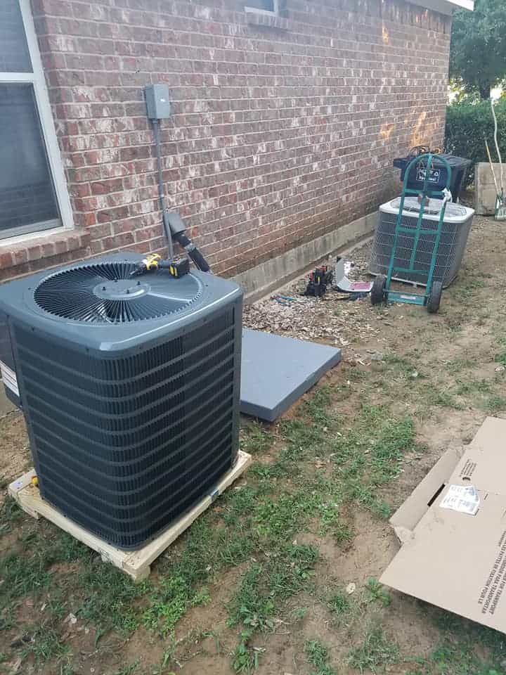New residential heat pump replacement with outdoor condenser unit installed on a concrete pad beside a brick home