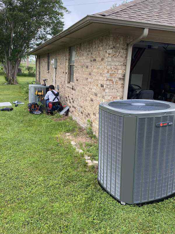 HVAC technician performing a residential heat pump replacement with new outdoor units installed beside a brick home
