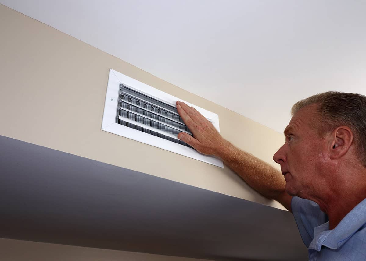 Homeowner testing heating vent air flow with hand