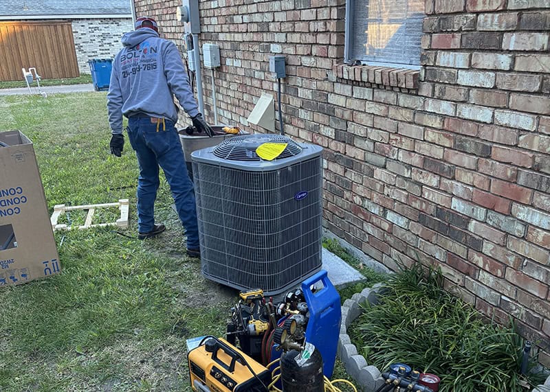 HVAC technician installing new air conditioning unit outside Dallas brick home with tools and equipment